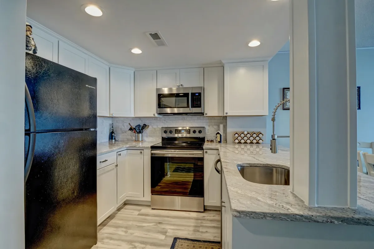 A warm, inviting kitchen featuring a black refrigerator, stainless steel stove, white cabinetry, and a granite countertop. The space is designed for cooking and entertaining, with ample work surfaces and a cozy, homey feel.