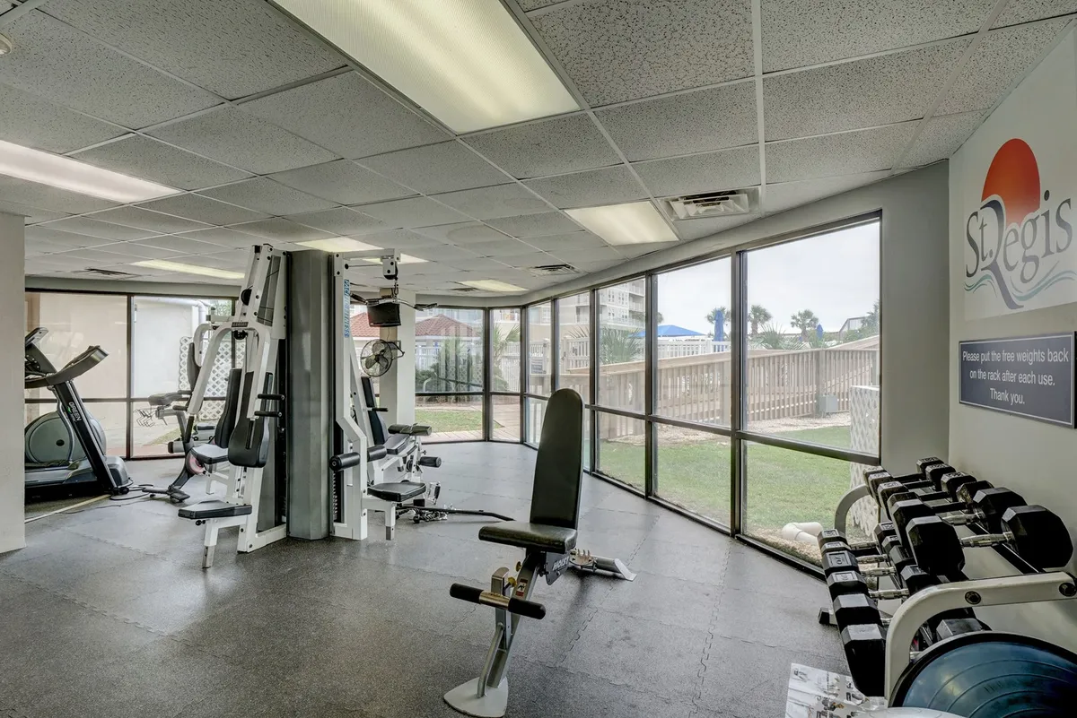 A spacious, modern fitness center filled with a variety of exercise equipment, illuminated by large windows that flood the room with natural light. The space invites motivation and health-focused activities, with areas for group fitness and personal training.