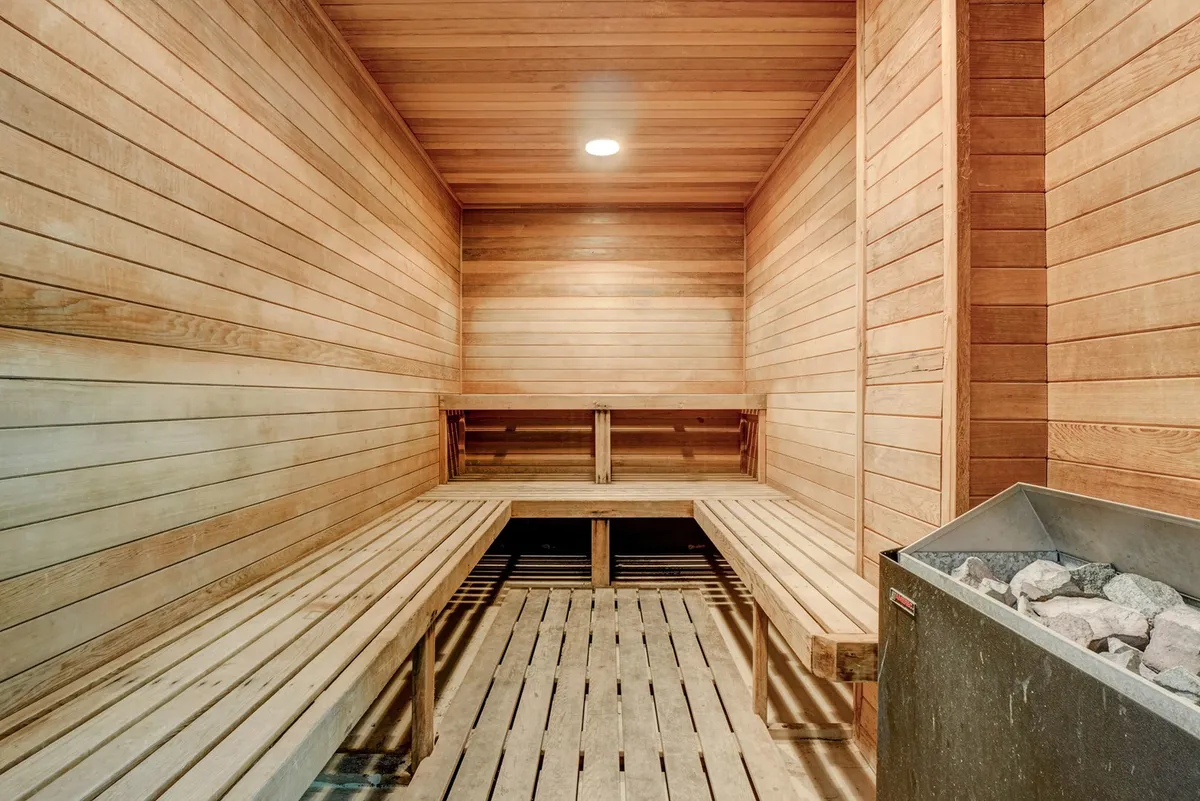 A tranquil sauna interior featuring wooden benches and a sauna heater, exuding warmth and relaxation. The inviting wood-clad space is designed for post-workout recovery, detoxification, and mindfulness.