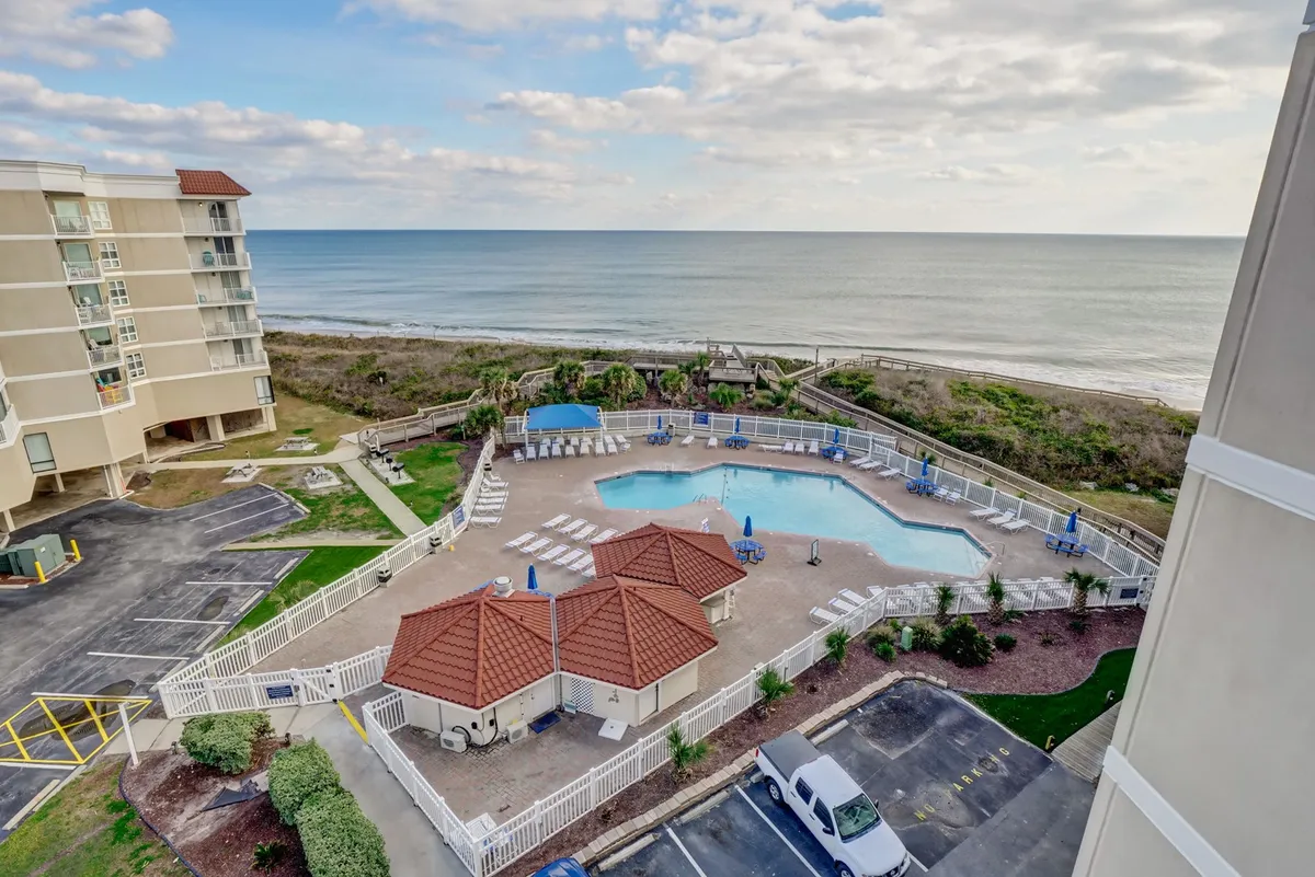 The image showcases the condo's sparkling saltwater pool surrounded by inviting beach chairs and cabana structures, all set against a stunning backdrop of the Atlantic Ocean. The gated pool area offers a tranquil atmosphere with panoramic ocean views, perfect for swimming, sunbathing, and relaxing while taking in breathtaking sunsets.