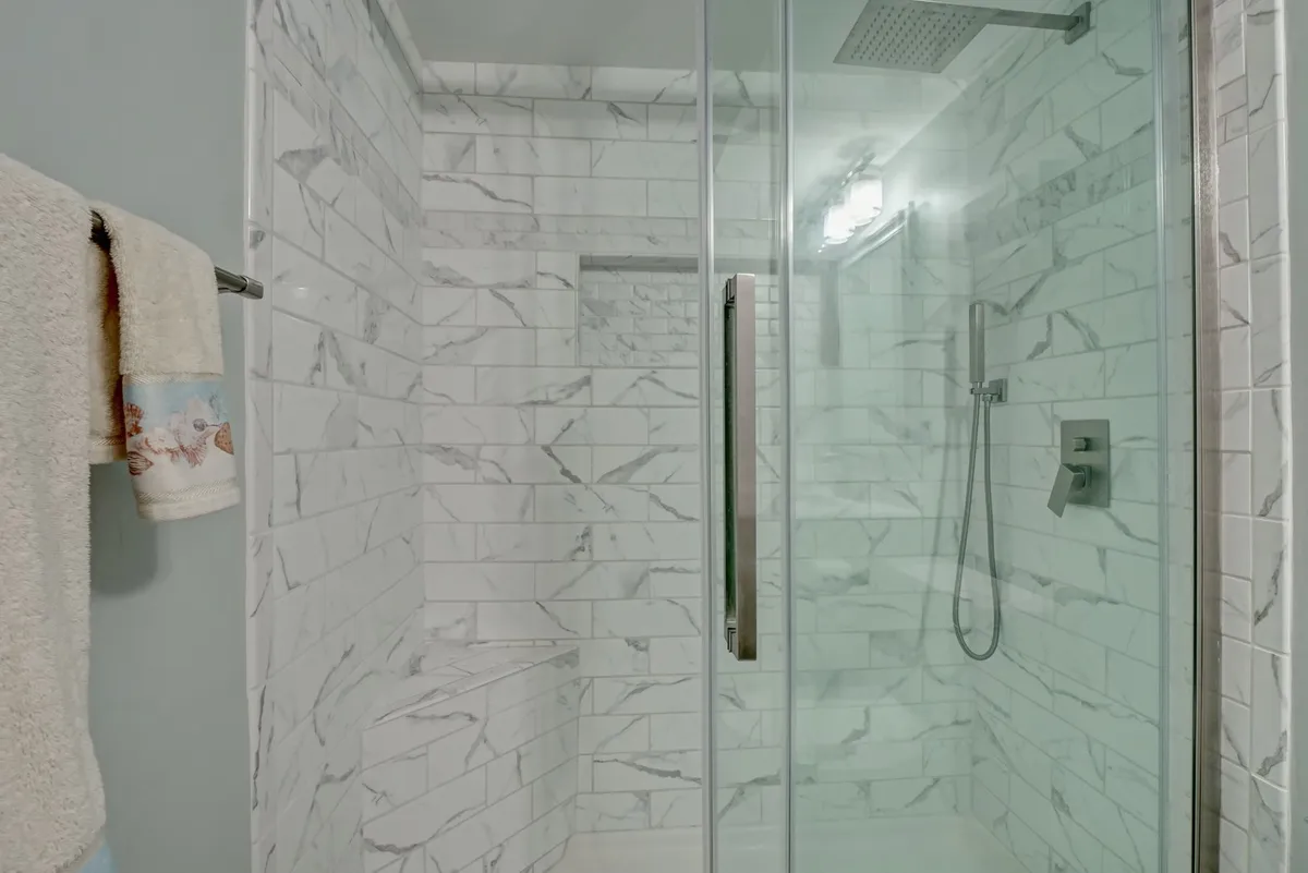 A modern bathroom with a glass-enclosed shower, sleek marble tile walls, and premium shower fixtures. The space feels invigorating yet tranquil, ideal for unwinding after a day’s adventure at the beach.