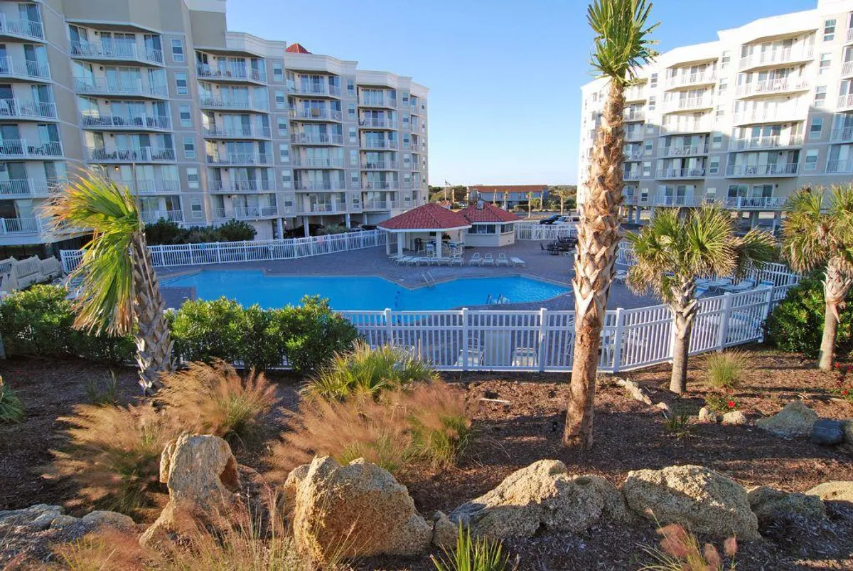 A lively pool area framed by palm trees and well-kept landscaping, with the building facade in the background. The scene radiates a welcoming, resort-style atmosphere ideal for family swims, sunbathing, and relaxing together outdoors.