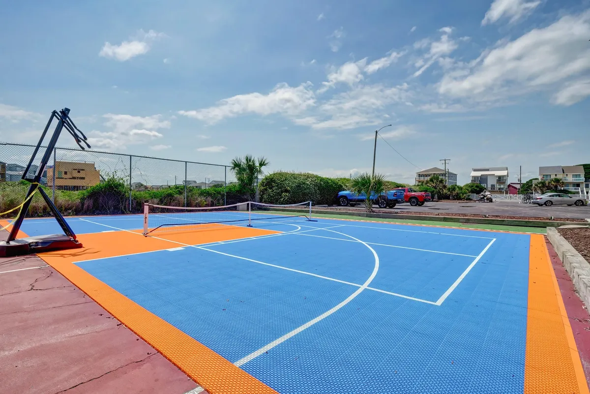 A vibrant outdoor sports court with a basketball hoop and tennis net, bordered by greenery. The surface is brightly colored and inviting, suggesting energy and activity. This image captures the spirit of active recreation available to guests, reinforcing the section’s nod to fitness and wellness routines.