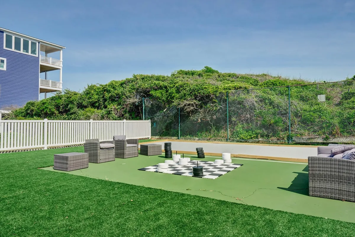 An inviting outdoor area featuring a giant chessboard set on a green lawn, with comfortable seating arranged nearby. The scene is lively yet relaxed, encouraging interactive play and conversation among friends.
