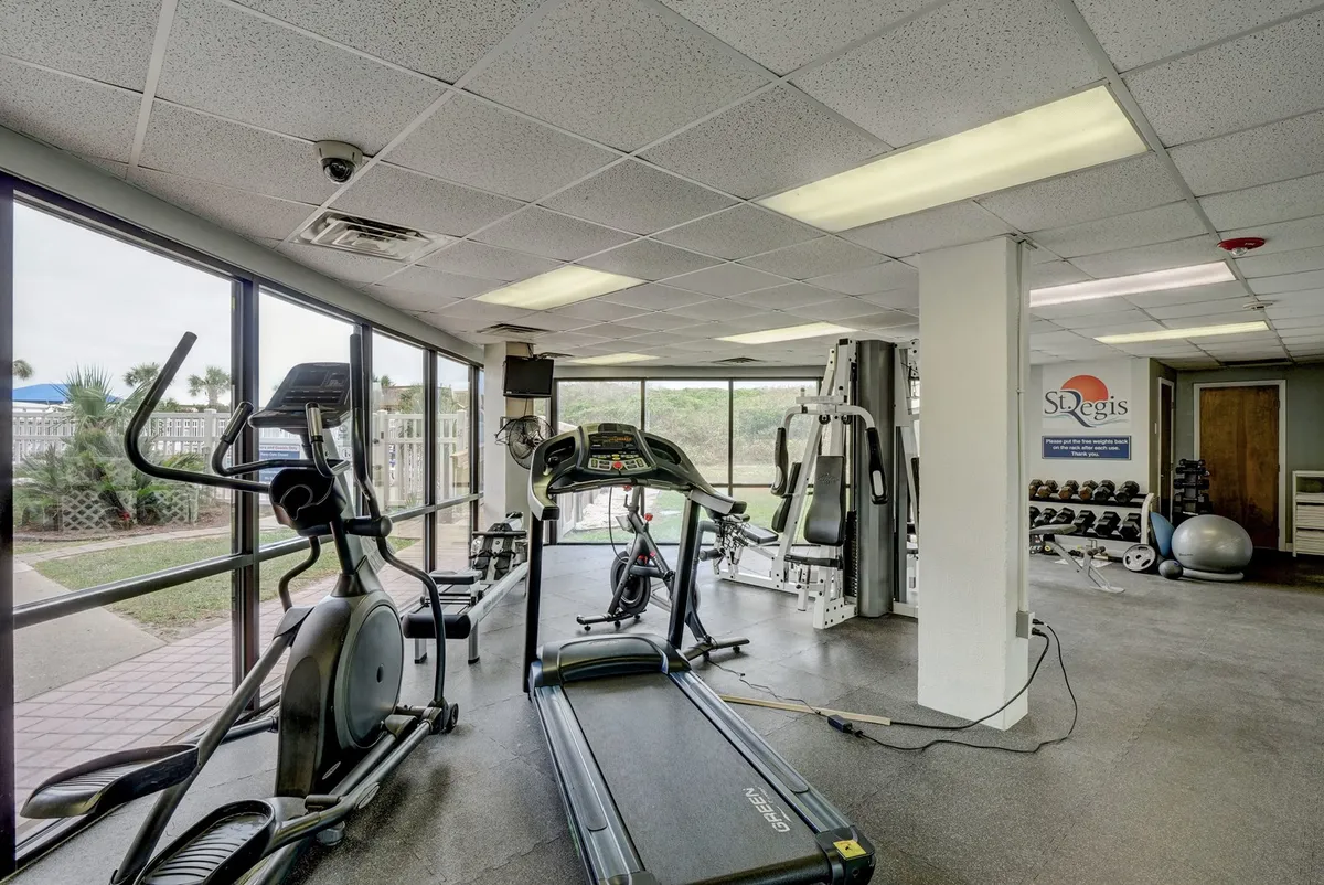 A bright, well-equipped fitness area featuring treadmills, ellipticals, weight training equipment, and large windows, all designed for dynamic workouts and group fitness sessions.