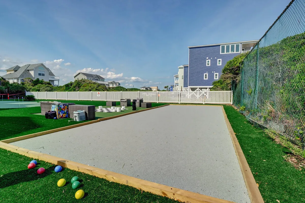 A bocce ball court with colorful balls spread across the gravel, surrounded by greenery and adjacent houses. The setting is casual and inviting, ideal for friendly competition and laughter-filled evenings.