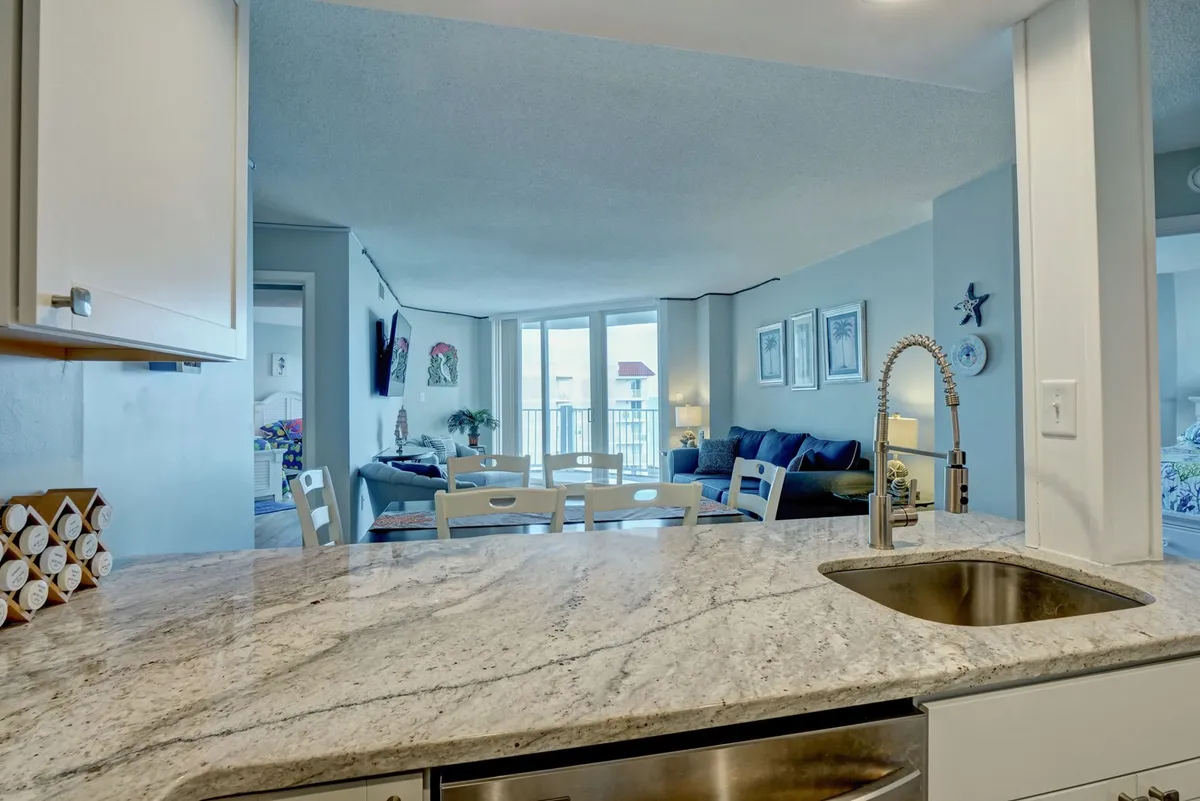 An interior view featuring a kitchen countertop, living room seating area, and large windows that let in abundant natural light. This inviting space is perfect for remote work, with upgraded interiors and easy access to relaxation. The windows suggest a connection to the outdoors, aligning with the section’s work/life balance narrative.